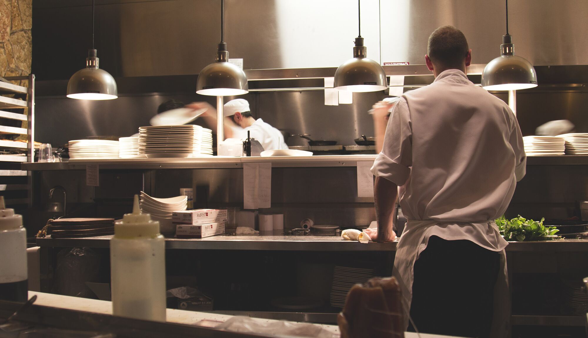 Cooks working the line in a large stainless-steel institutional kitchen